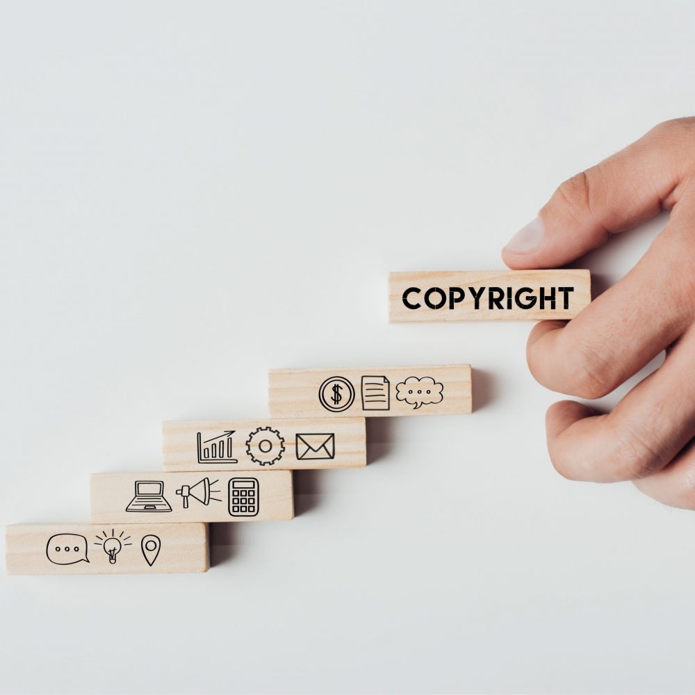 cropped view of man holding wooden block with word 'copyright' on top of wooden bricks with icons